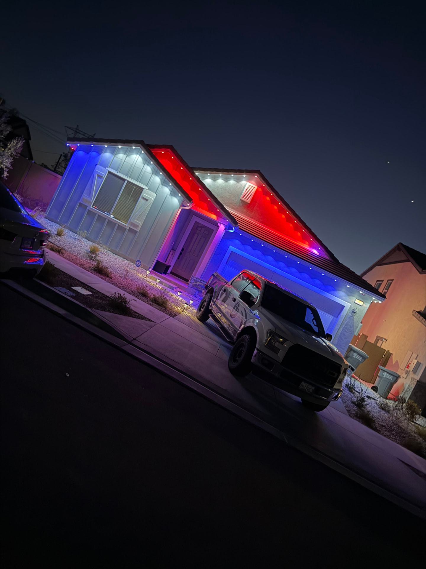 Single-story home lit in red, white and blue permanent LED roofline lighting with work truck in the driveway