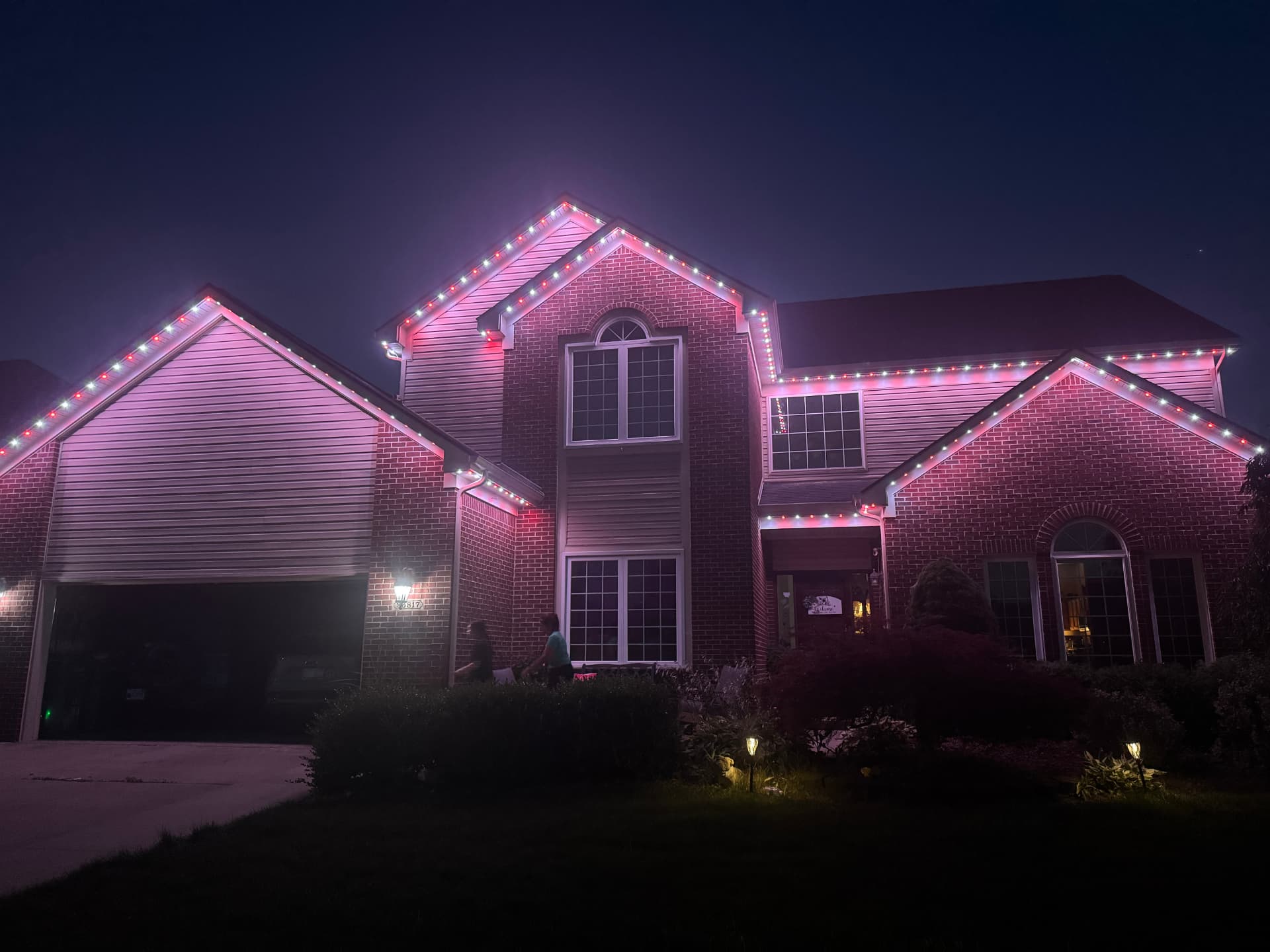 Brick home with pink and red permanent LED roofline lighting at night